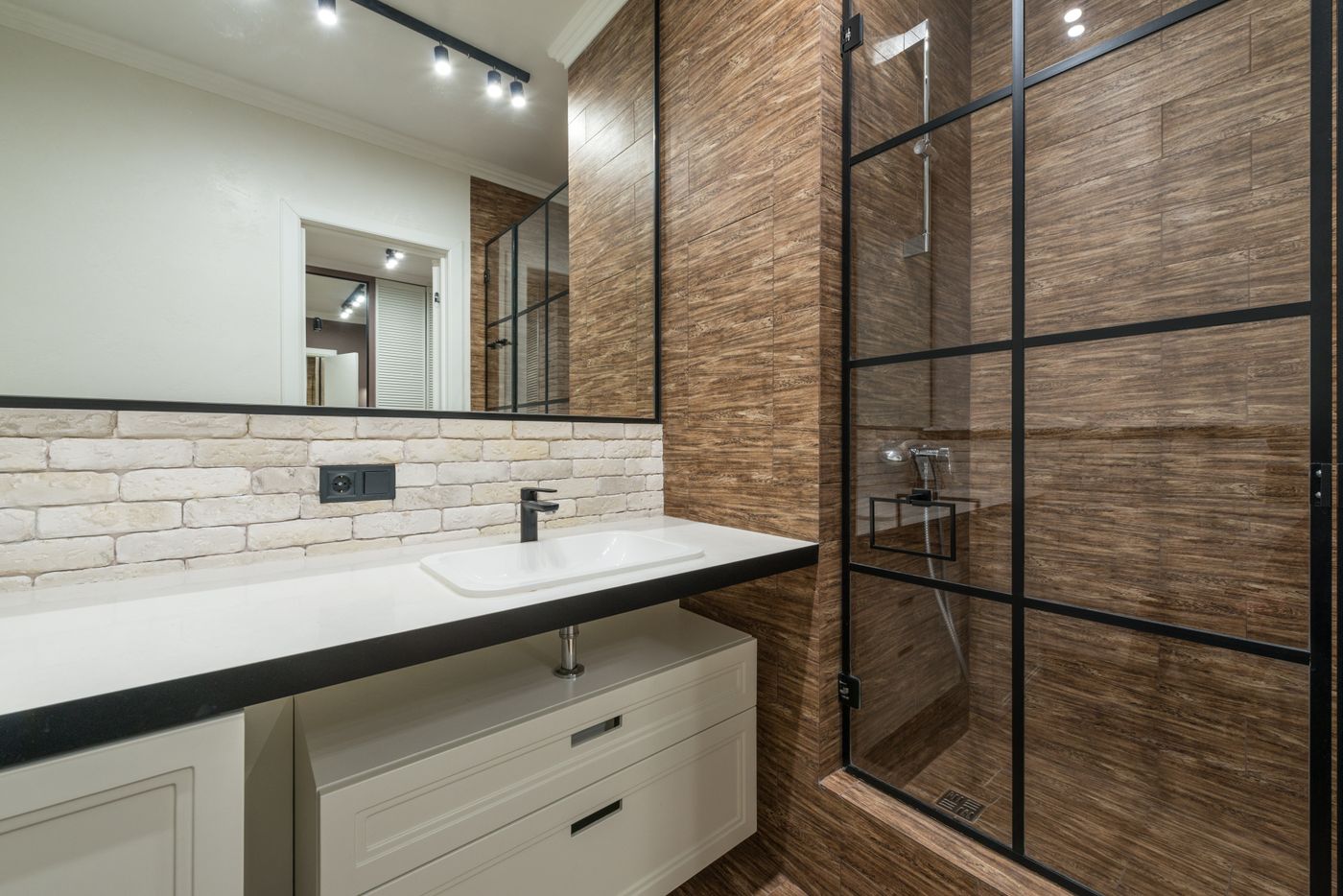 Photograph of a bathroom basin and walk-in shower with black metal framing